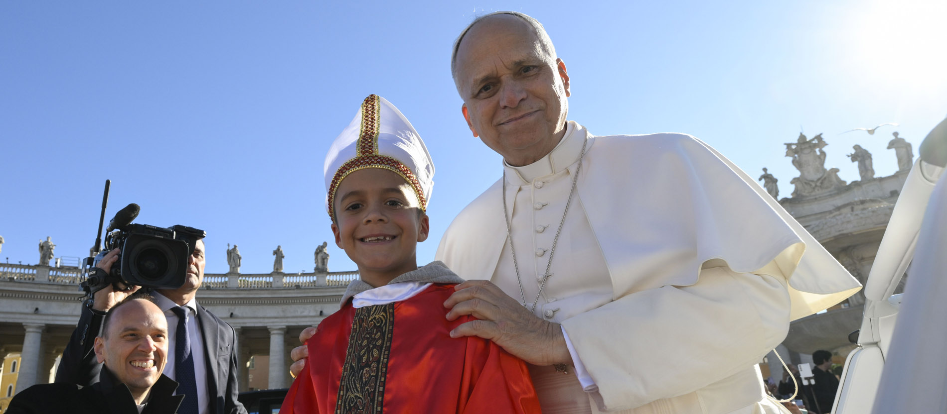 Papst Leo XIV. steht neben einem Kind. Das KInd sieht aus wie ein Mini-Papst.