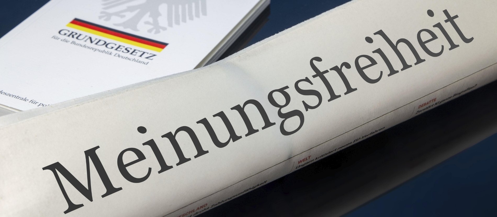 Symbolische Zeitung mit der Schlagzeile MEINUNGSFREIHEIT, im Hintergrund das deutsche Grundgesetz