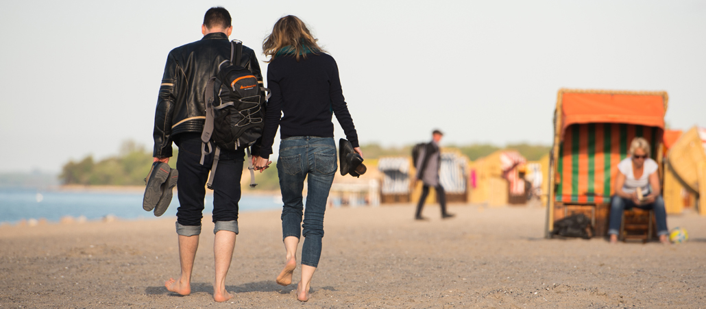 Ein Paar geht Hand in Hand am Strand entlang.