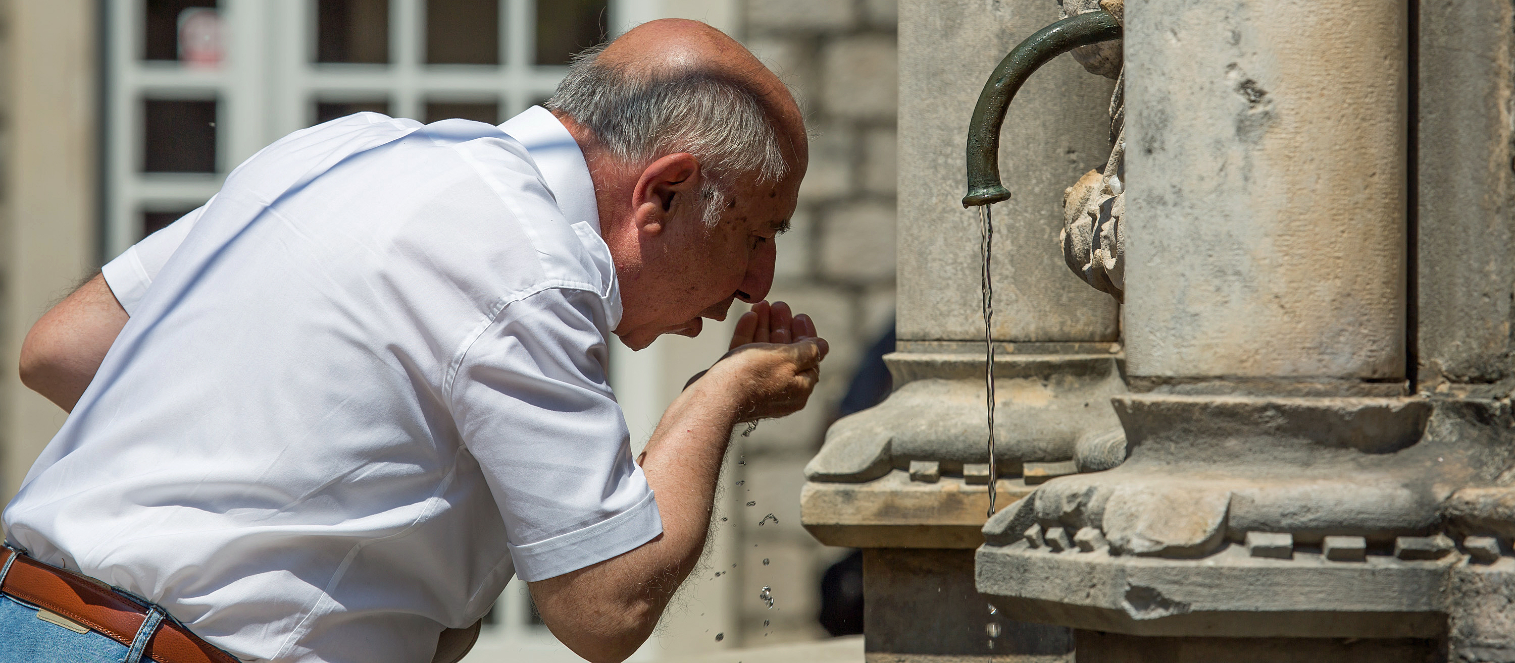 Mann trinkt an Brunnen