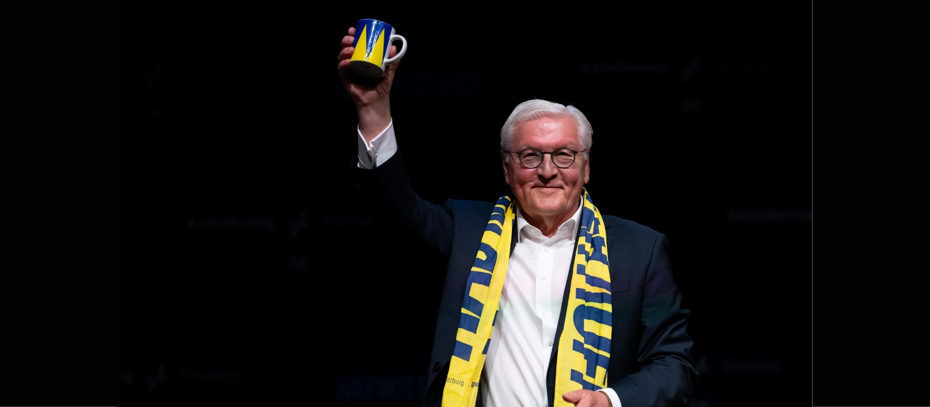 Bundespräsident Frank-Walter Steinmeier hält eine Tasse vom Katholikentag in die Höhe, die er zuvor geschenkt bekommen hat.