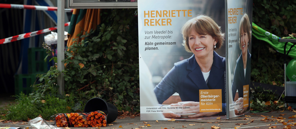 Ein Plakat der Kölner Obermeisterkandidatin Henriette Reker und umgefallene Rosen-Kübel sind am 17.10.2015 in Köln am Tatort zu sehen.