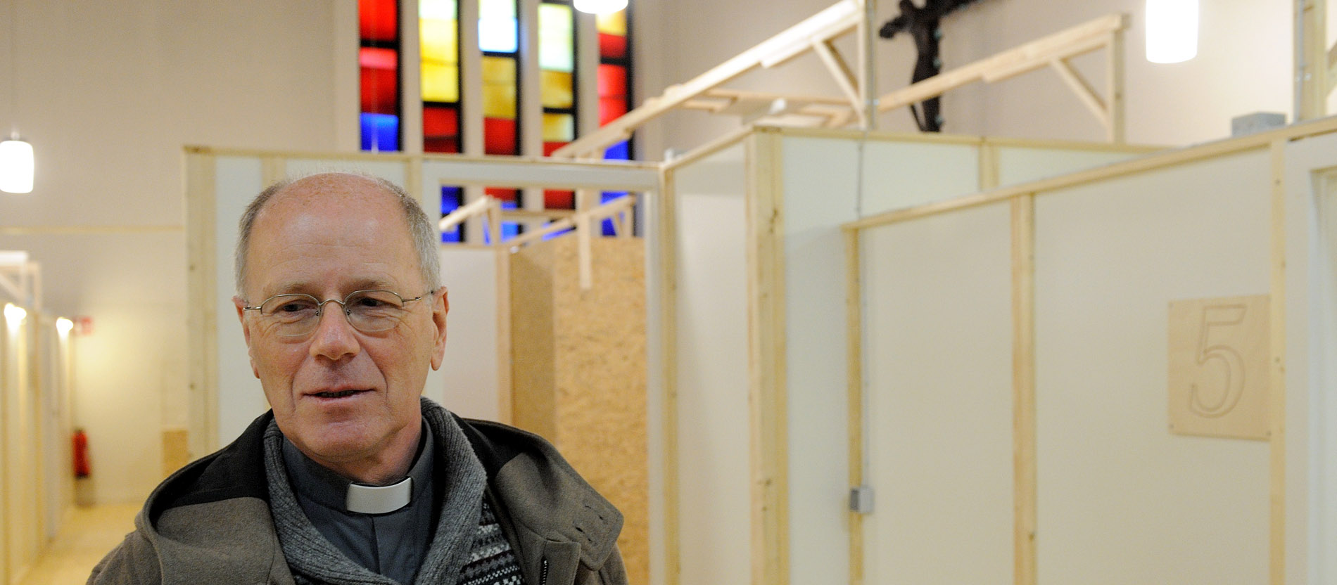 Eine Pfarrer in einem mit Holzwänden verbauten Innenraum einer Kirche.