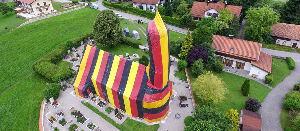Die Kirche Sankt Coloman in Kirchseeon ist für eine Holzwurm-Bekämpfung in eine Folie in den Farben Schwarz, Rot und Gold gehüllt.