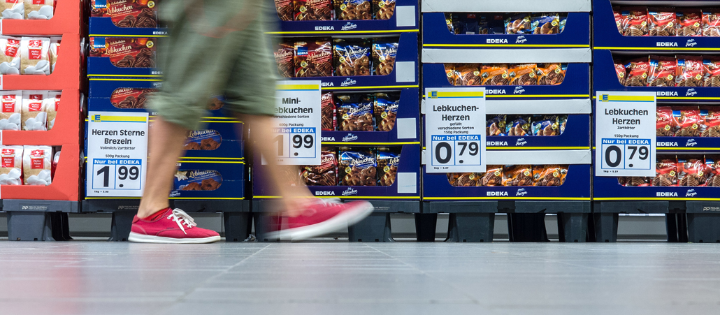 Paletten mit Lebkuchen in einerm Supermarkt, davor läuft ein Mann in kurzer Hose.