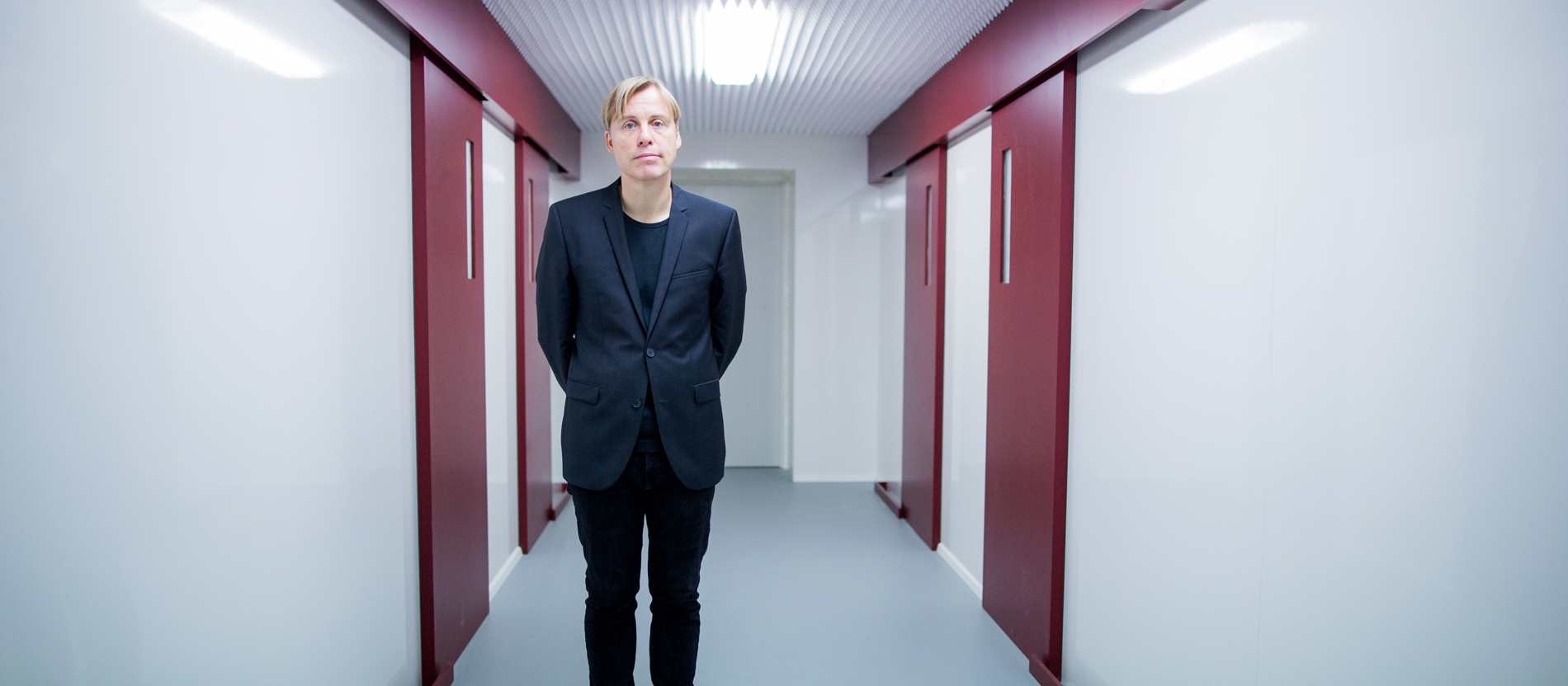 Der Künstler Gregor Schneider steht in einem Raum mit vier roten Türen.