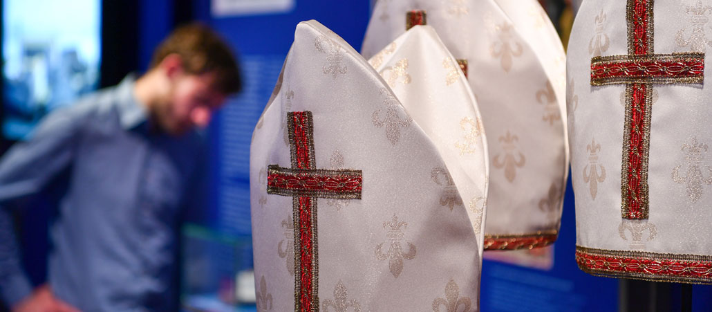 Mehrere Mitren, dahinter schaut interessiert ein Mann