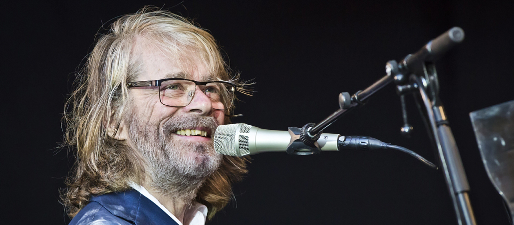 Der Musiker Helge Schneider sitzt vor einem Mikrofon und lacht.