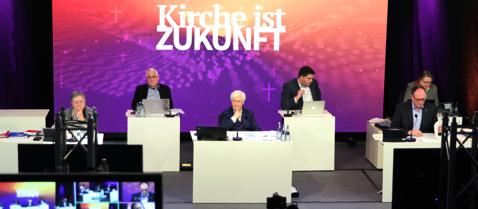Drei Frauen und drei Männer sitzen vor einem Bildschirm mit der Aufschrift "Kirche ist Zukunft"