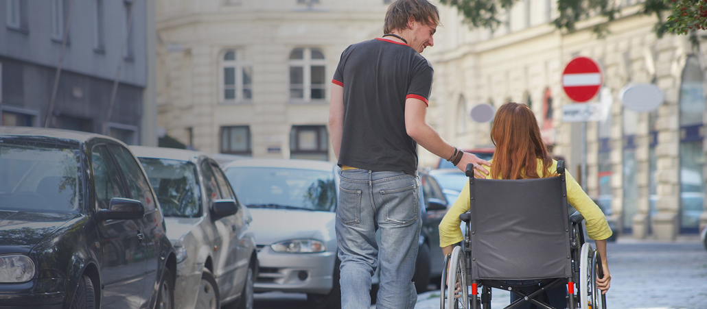Ein junger Mann ist mit einer jungen Frau unterwegs, die im Rollstuhl sitzt.
