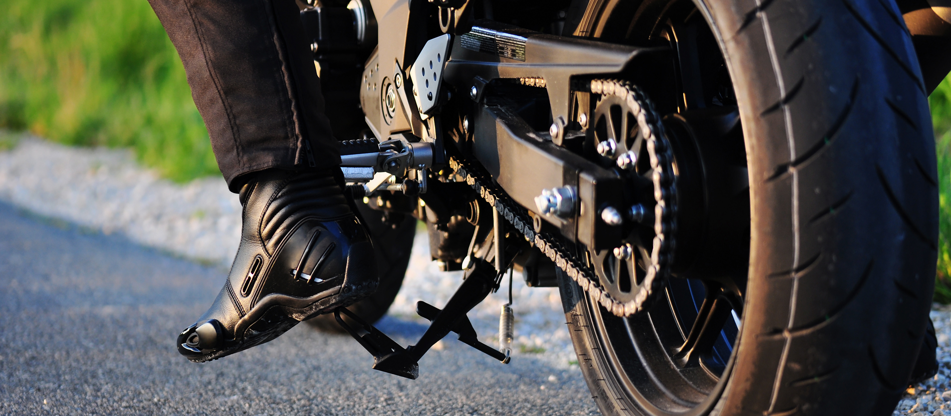 Der Hinterreifen eines Motorrads steht auf dem Asphalt. Am linken Bildrand sieht man noch den Fuß des Fahrers in seinem schweren Stiefel.