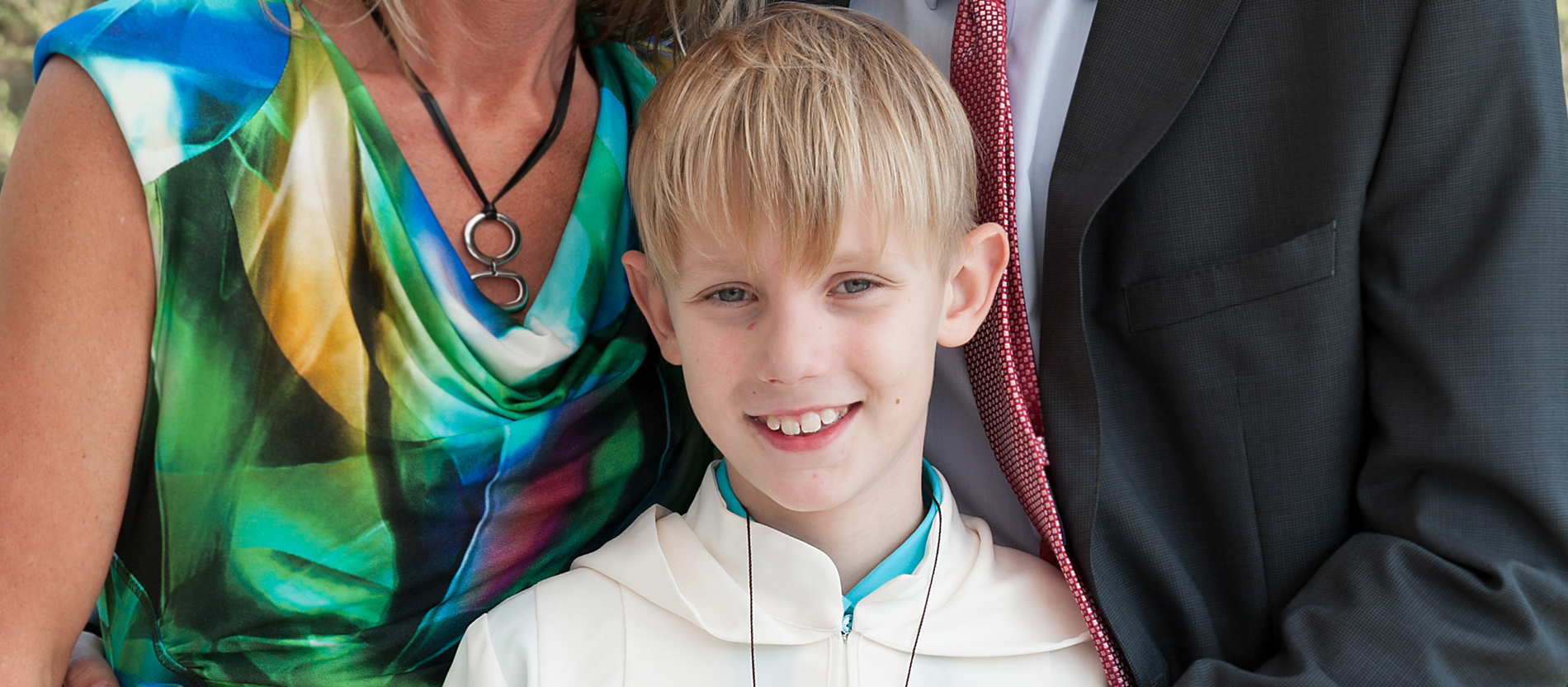 Eltern posieren mit ihrem 9-jährigen Sohn für ein Foto. Der blonde Junge trägt sein Erstkommuniongewand.