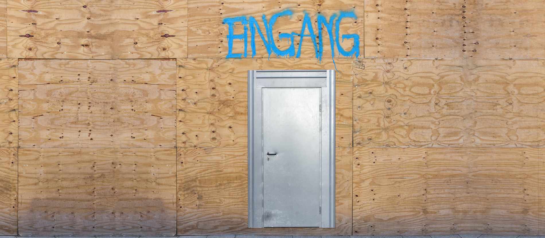 Ein einer Holzwand ist eine Eingangstür eingelassen.