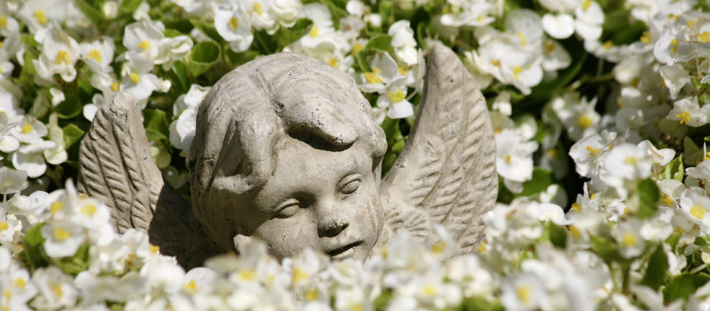 Ein Steinengelchen zwischen Blüten auf einem Friedhof.