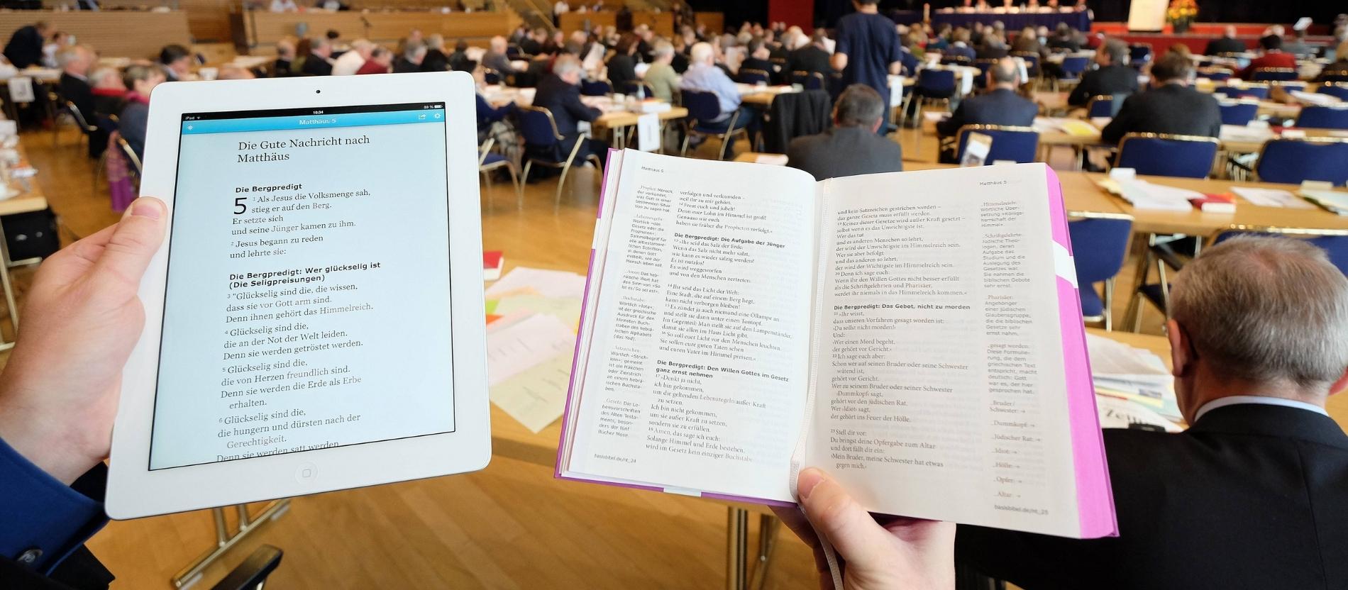 Ein Mann hält ein iPad und eine Bibel mit dem Matthäus-Evangelium
