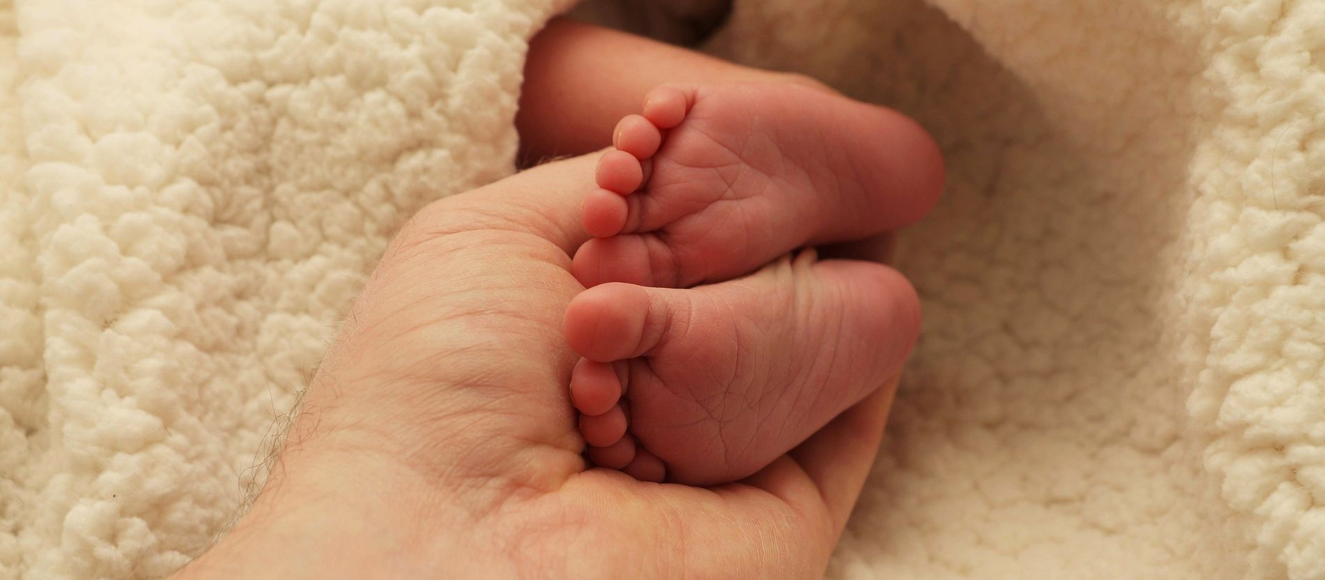 Zwei Babyfüße ragen aus einer weißen Wolldecke.
