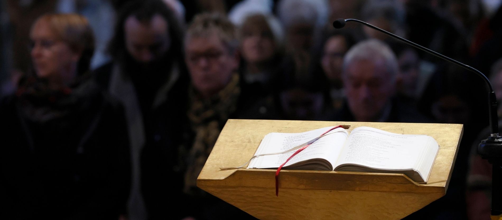 Ein Evangeliar liegt auf einem Ambo, im Hintergrund die Gläubigen in der Kirche