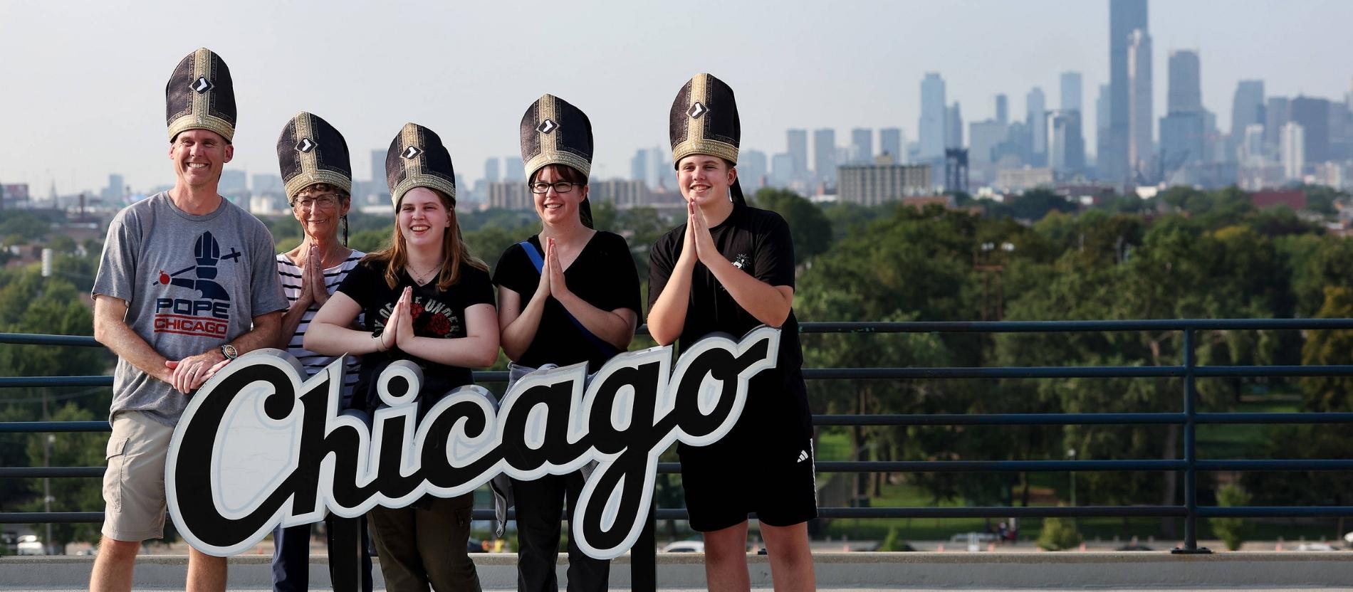 Baseballfans stehen für ein Gruppenfoto hinter einem Chicago-Schriftzug, auf dem Kopf tragen sie Mitren
