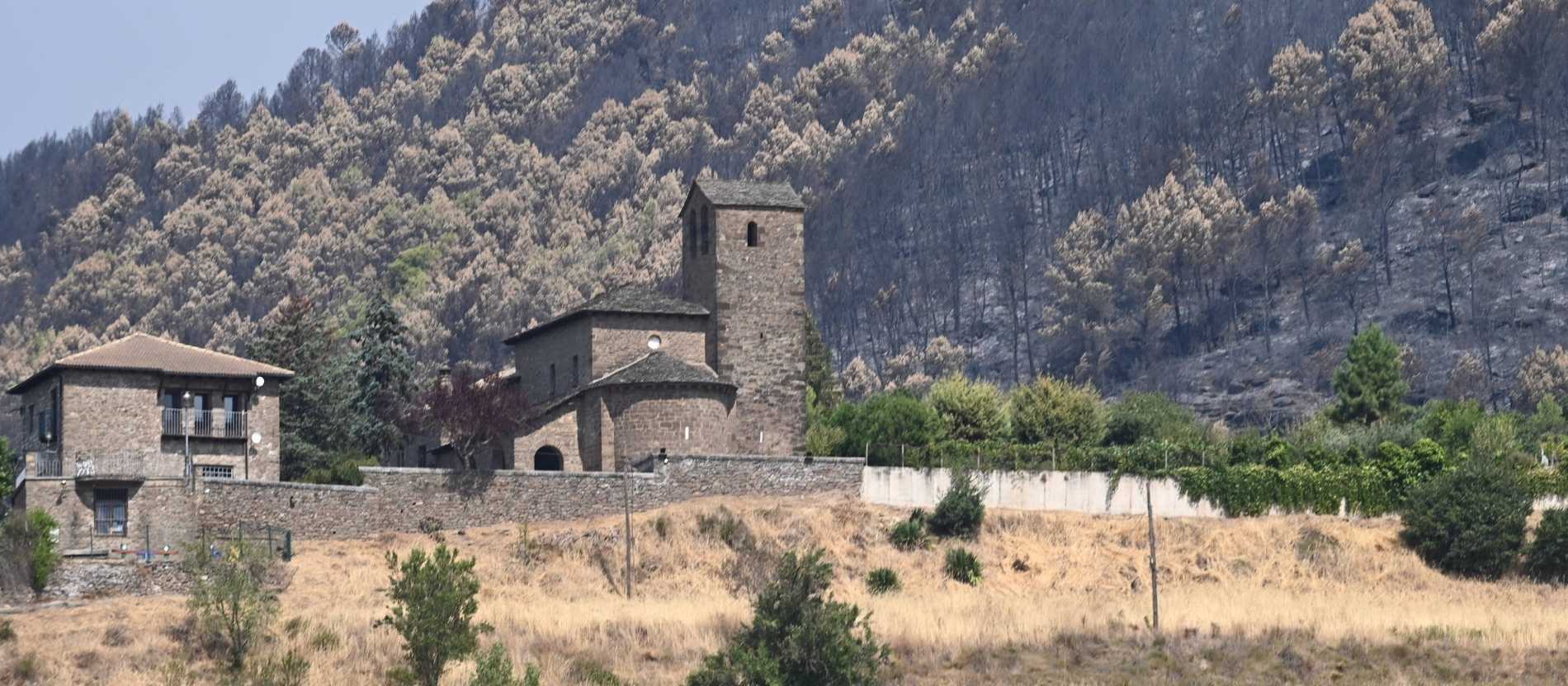 Die Klosteranlage San Juan de la Peña in Spanien neben abgebrannten Bäumen an einem Hang.