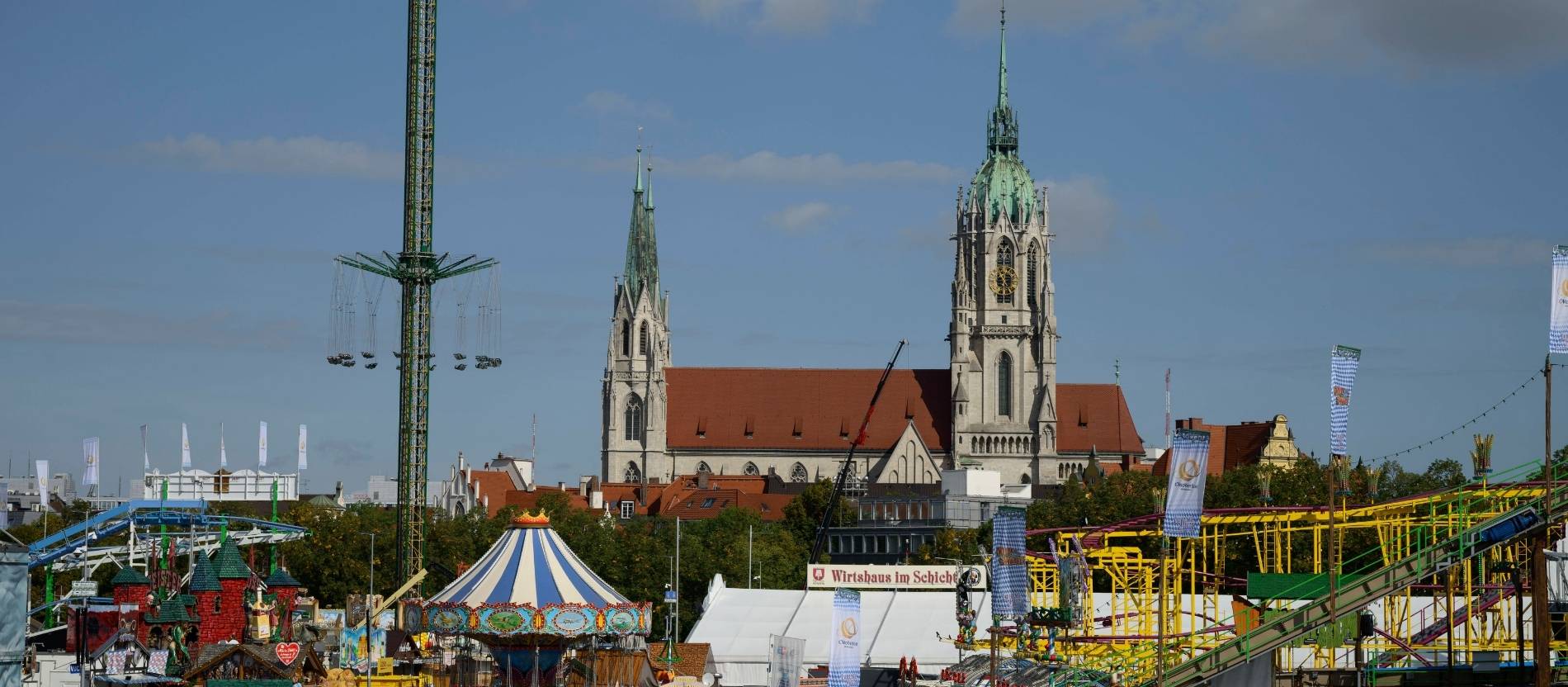 Die Kirche Sankt Paul in München, im Vordergrund Fahrgeschäfte des Oktoberfests