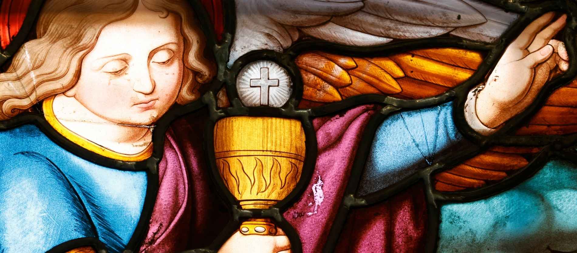 Auf einem Kirchenfenster hält ein Engel die Eucharistie