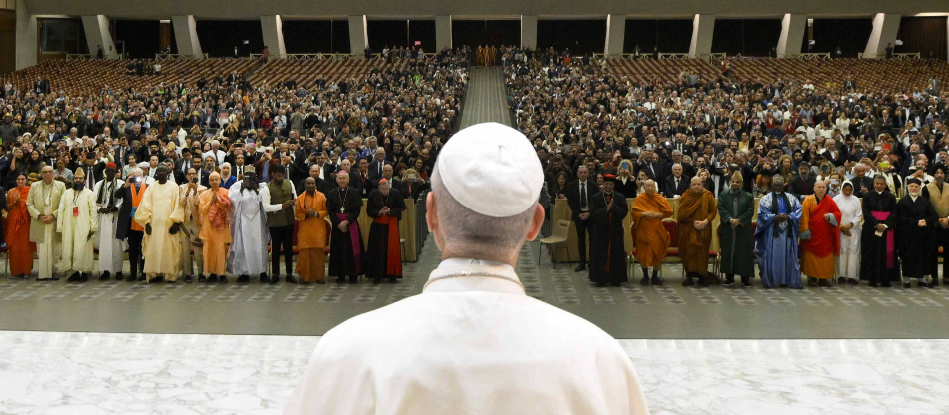 Papst Leo steht mit dem Rücken zur Kamera. Vor ihm sind Menschen verschiedenster Religionen