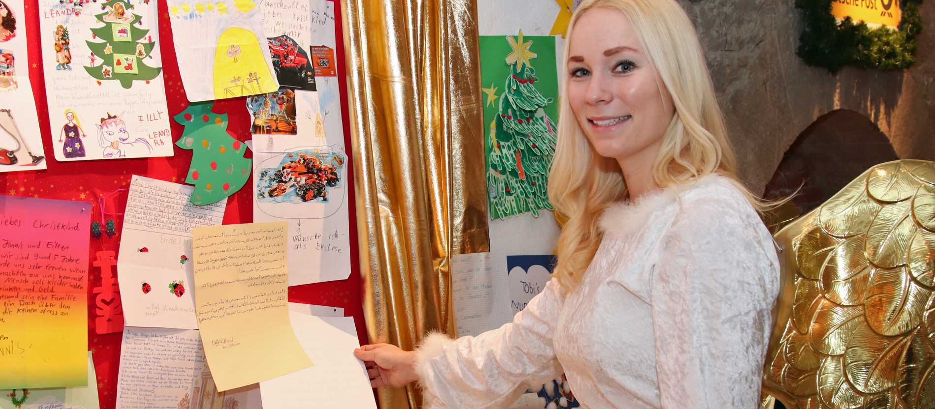 Das Christkind steht vor einer Wand mit Briefen.