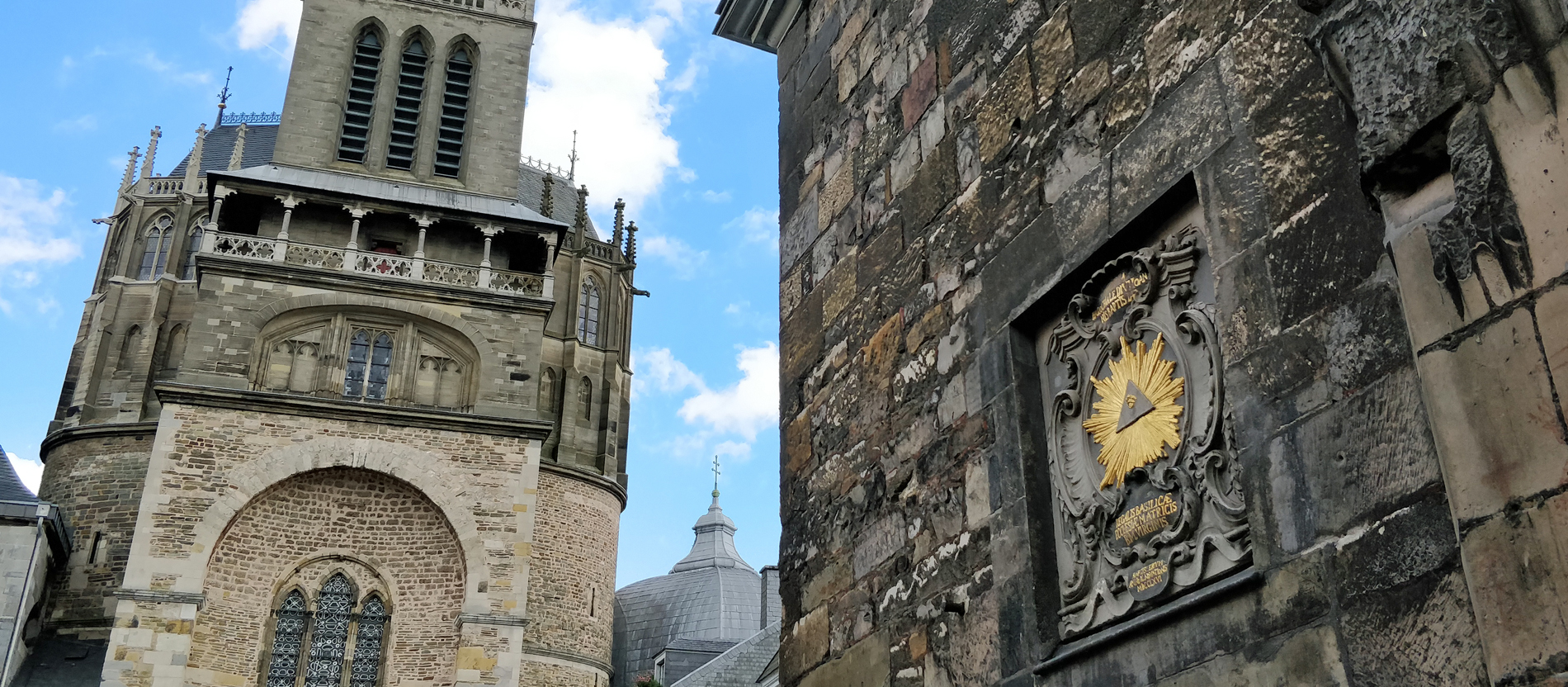 Links sieht man den Aachener Dom, rechts die Taufkapelle mit dem Symbol 