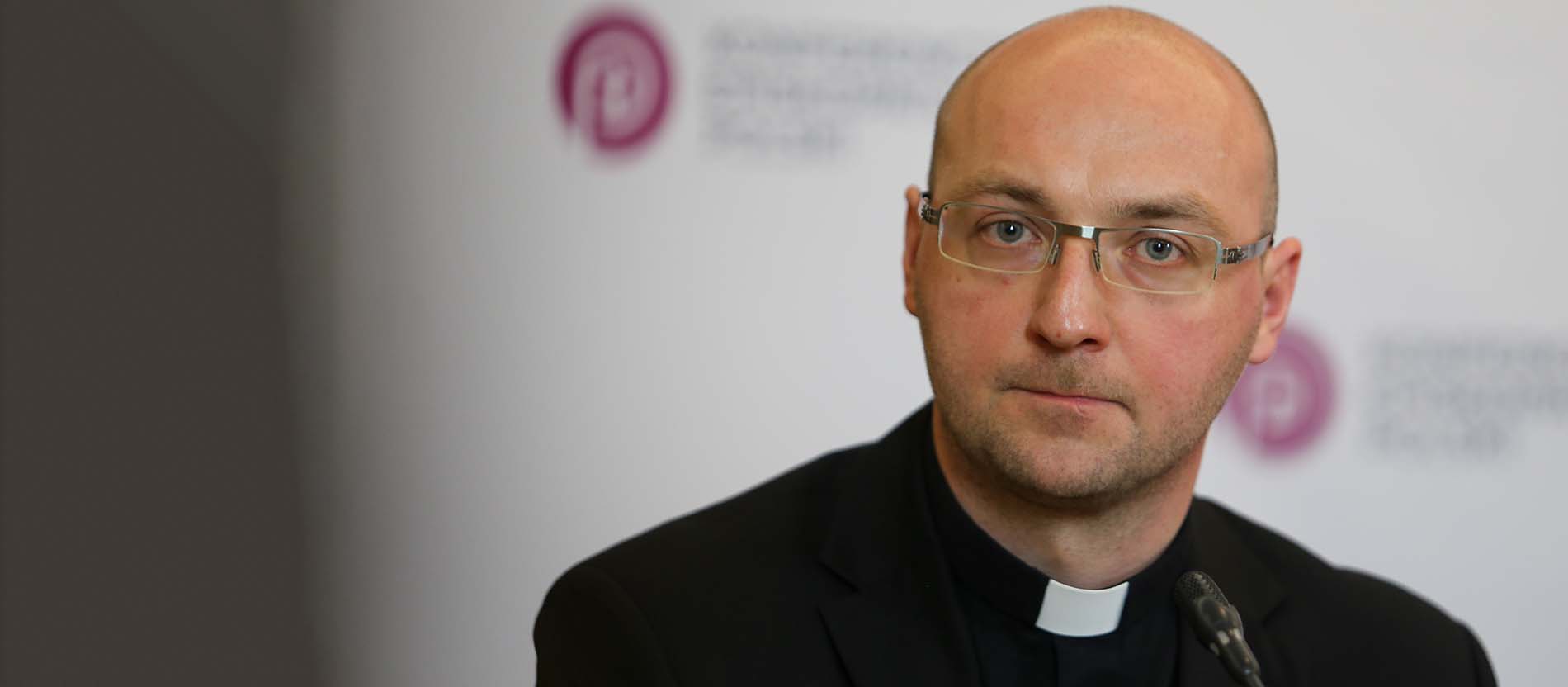Porträt von Piotr Studnicki vor dem Logo der Polnischen Bischofskonferenz