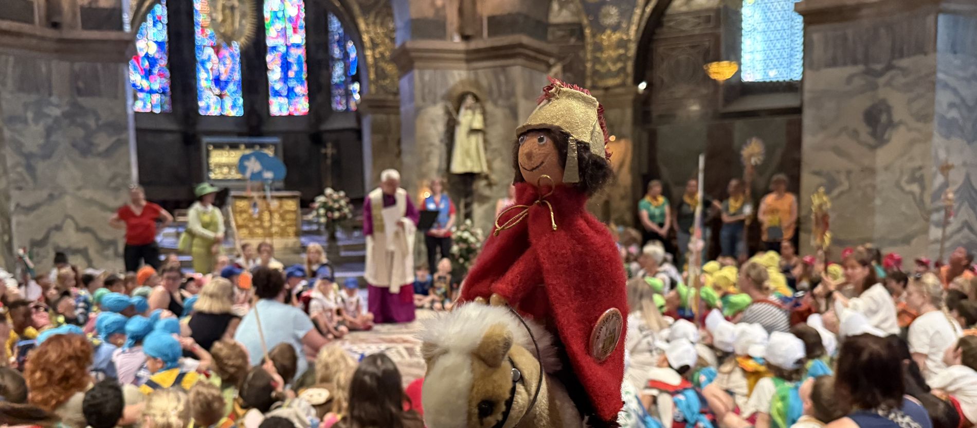 Pilgerstab-Puppe im Vordergrund, dahinter Domkapitular und Kinder beim Gottesdienst im Aachener Dom