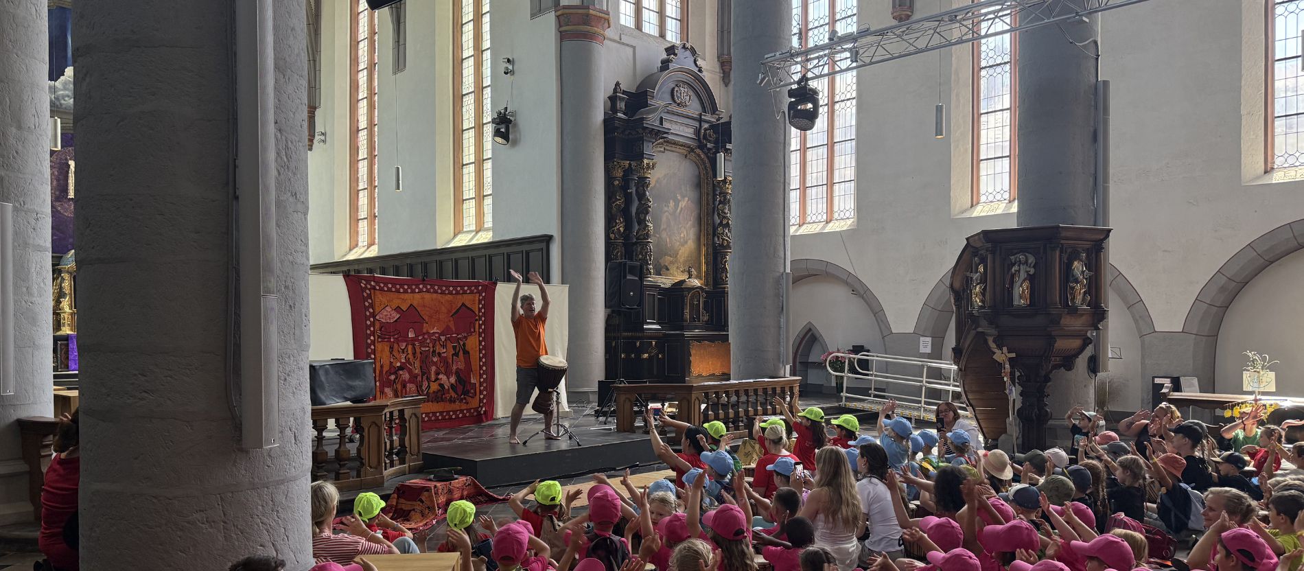 Kinder in bunten Mützen klatschen und tanzen bei einer Trommelvorführung beim Kinderpilgertag in Aachen