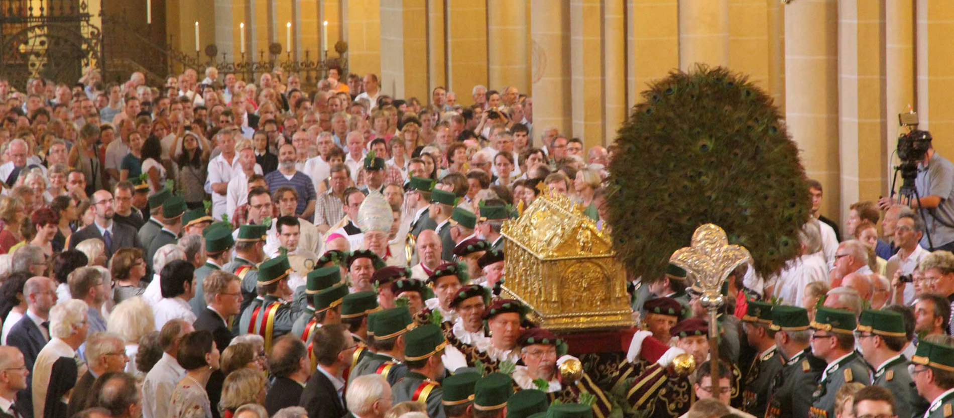 Ein goldener Schrein wird durch eine vollbesetzte Kirche getragen.