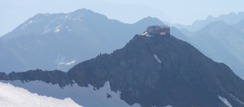 Blick auf ein Schneefeld in den Bergen mit einem Felsen, auf dem ein Haus gebaut ist