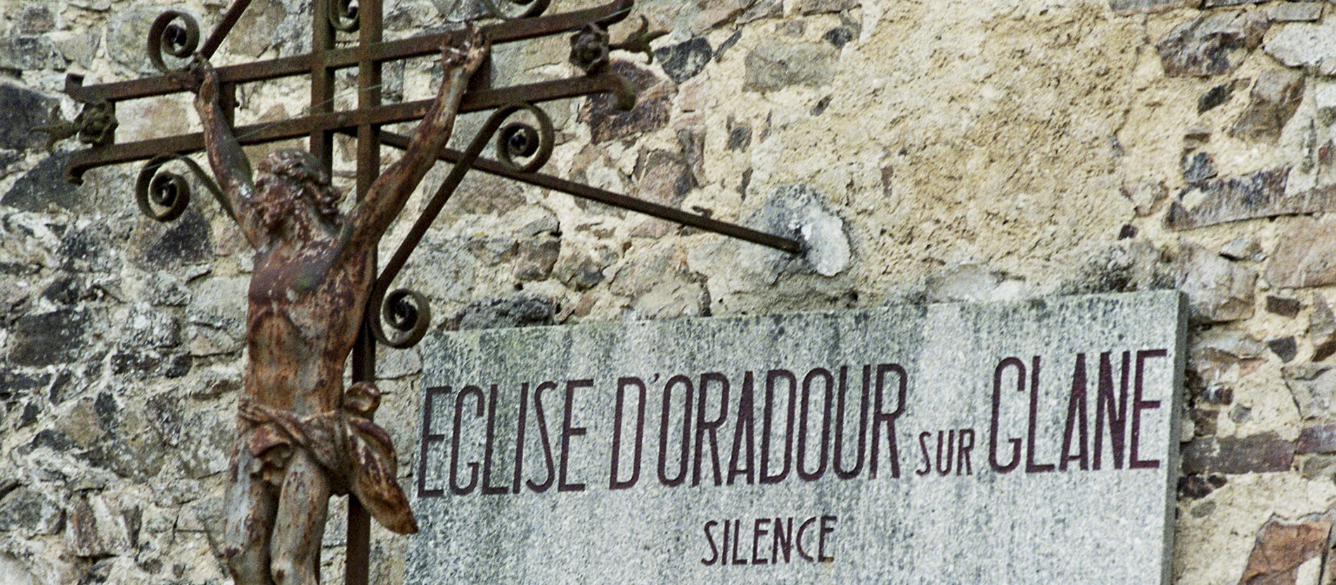 Ein rostiges Kruzifix und eine Gedenktafel in der Kirche von Oradour-sur-Glane.