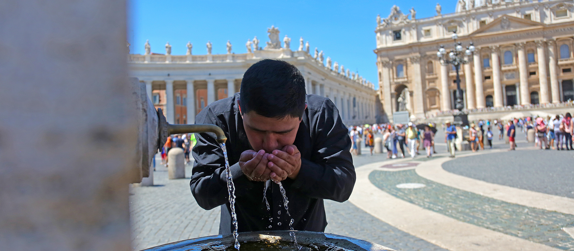Ein junger Priester trinkt am heißen Sommertag auf dem Petersplatz im Vatikan aus einem Brunnen.