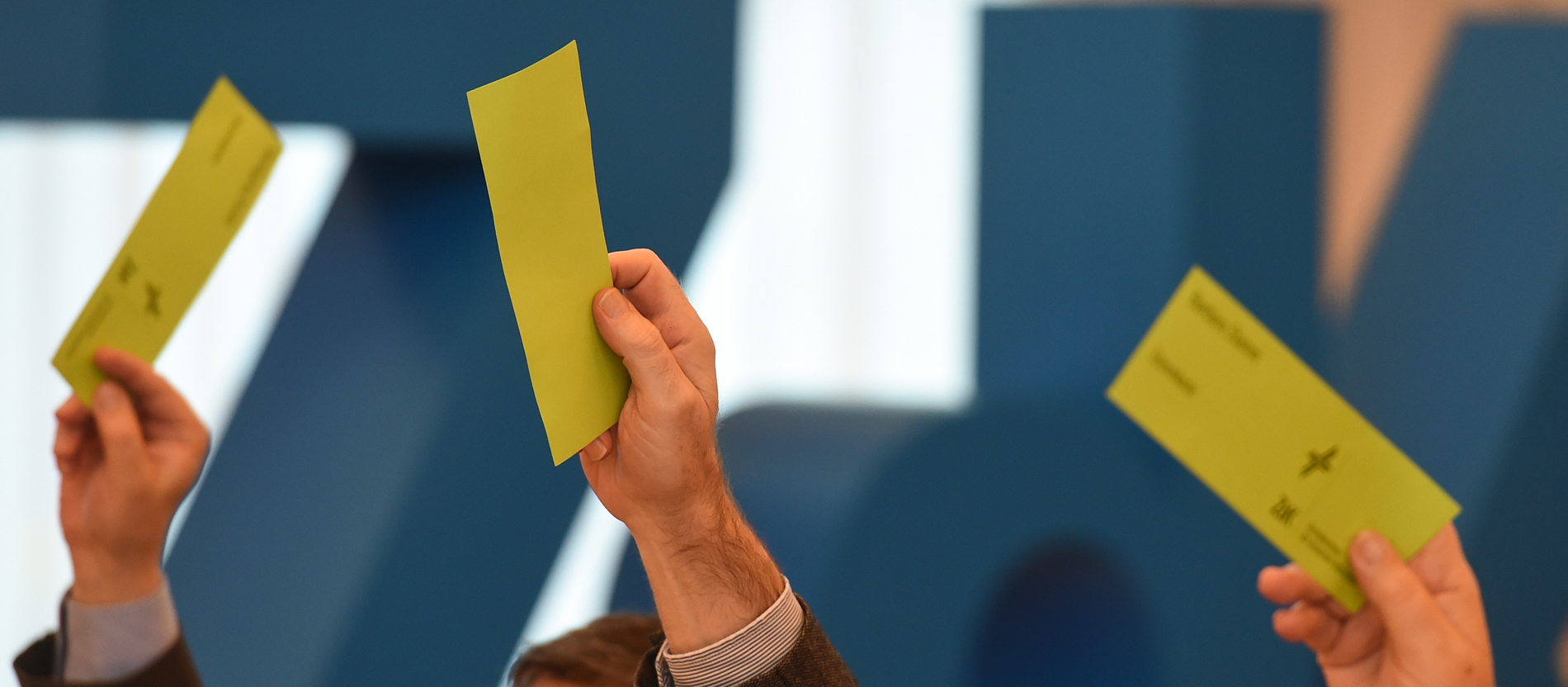 Drei hellgrüne Stimmzettel werden vor einem großen blauen ZdK-Logo hochgehalten.