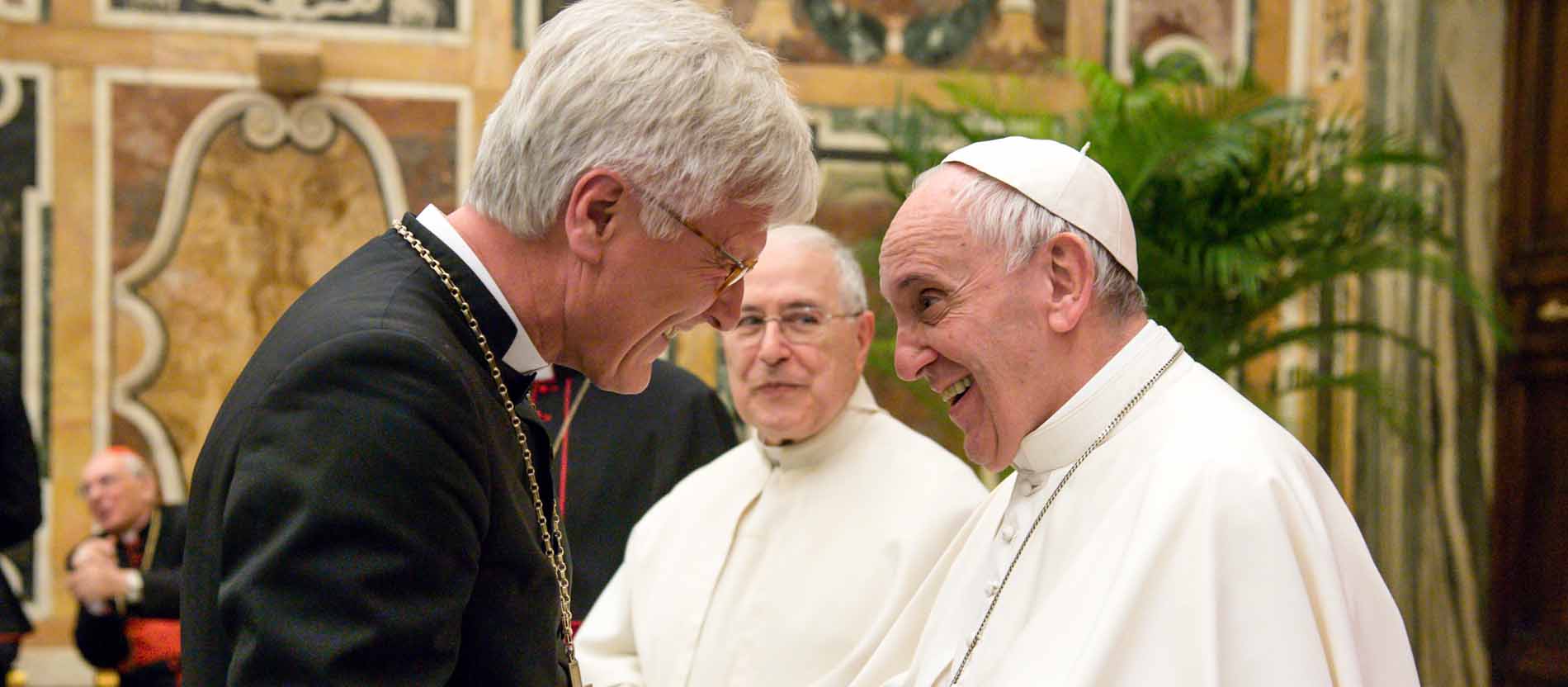 Heinrich Bedford-Strohm und Papst Franziskus geben sich lächelnd die Hand