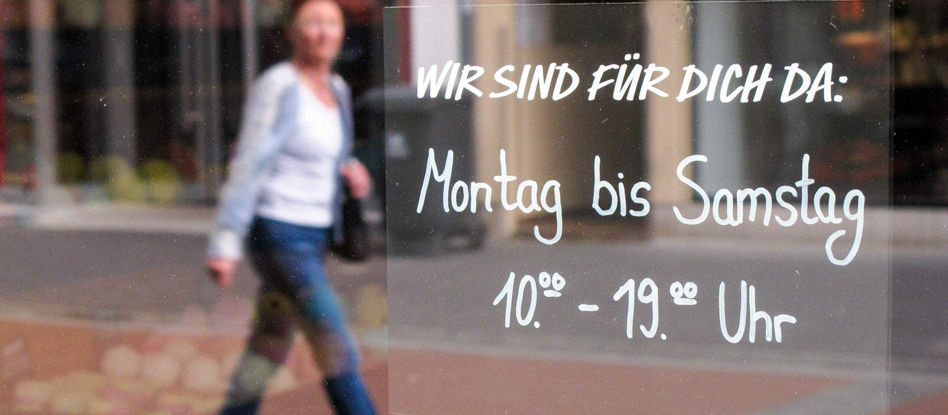 Ein Aufkleber mit der handschriftlichen Aufschrift "Wir sind für Sie da: Montag bis Samstag 10:00 bis 19:00 Uhr" auf einem Schaufenster