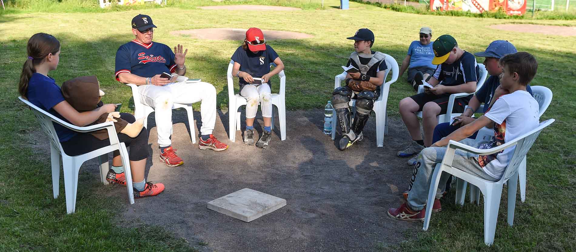 Junge Baseballspieler sitzen auf Stühlen und haben Bibeln in der Hand.