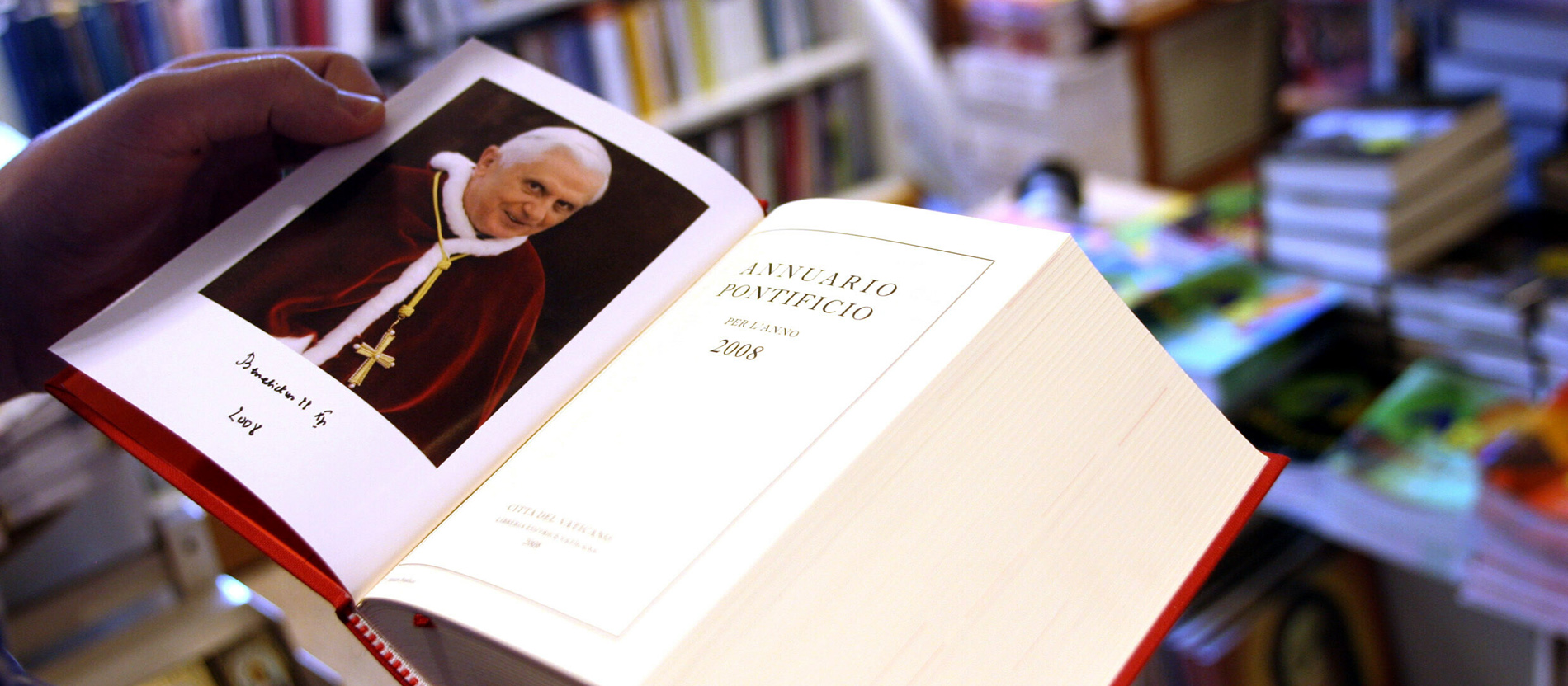 Ein Mann in einer Buchhandlung hält das päpstliche Jahrbuch aufgeschlagen in Händen.