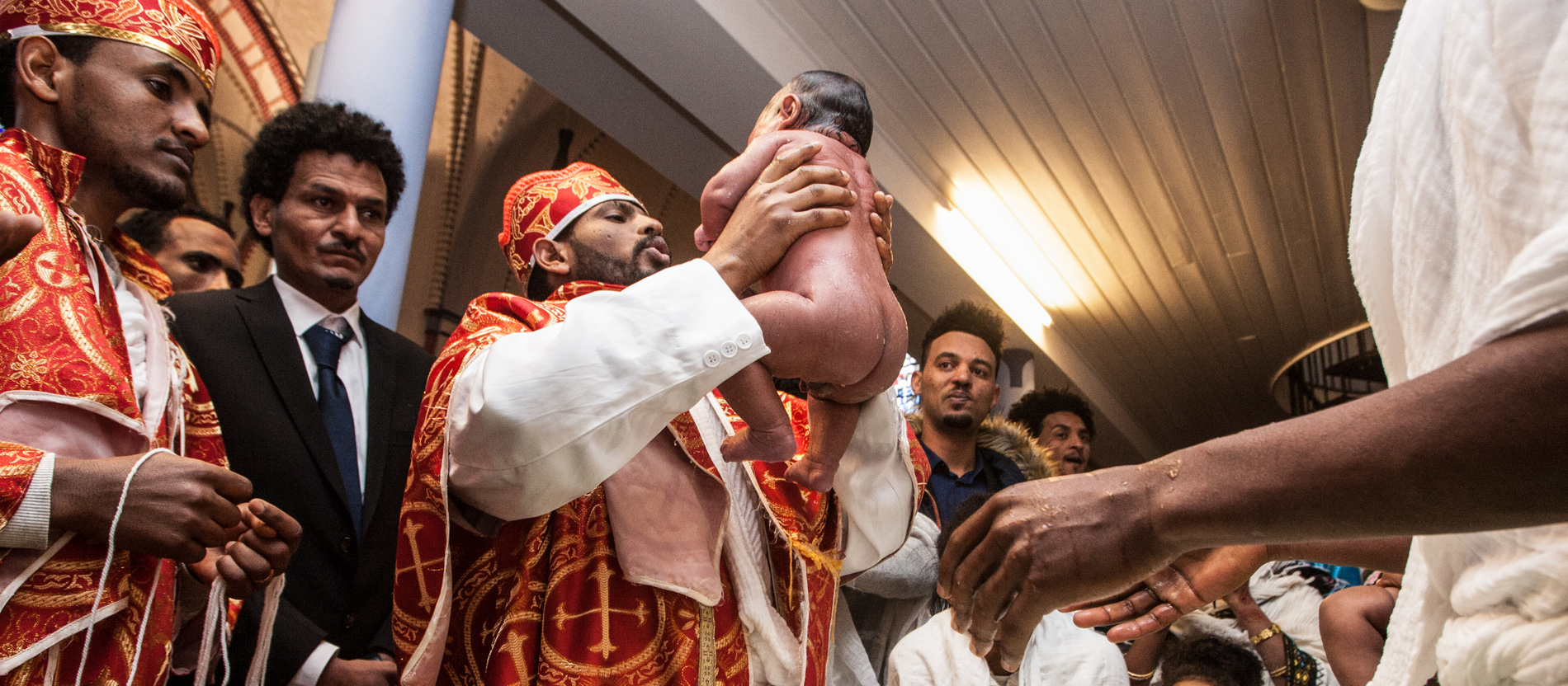 Ein Priester hält einen nassen, nackten Säugling in die Höhe