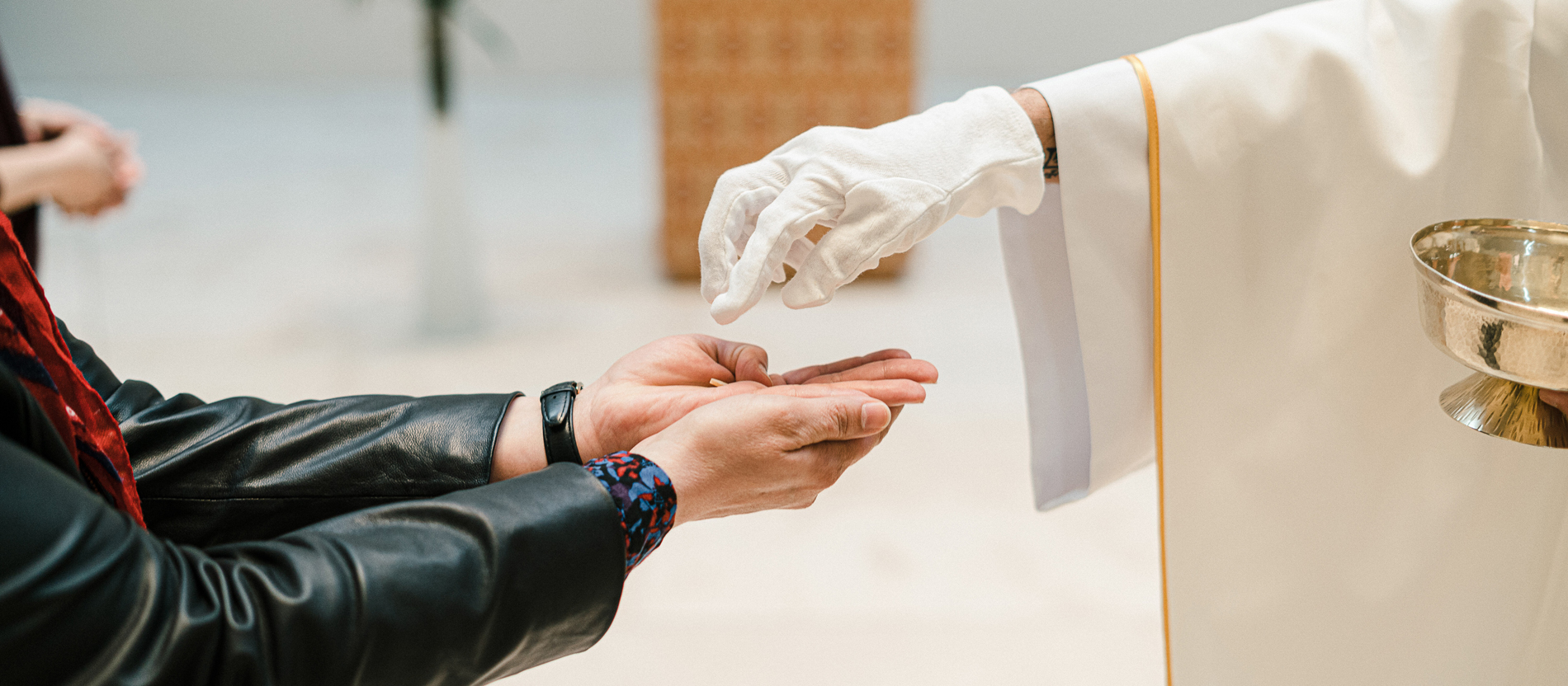 Ein Kaplan spendet einer Frau mit ausgestrecktem Arm und Handschuhen die Kommunion.