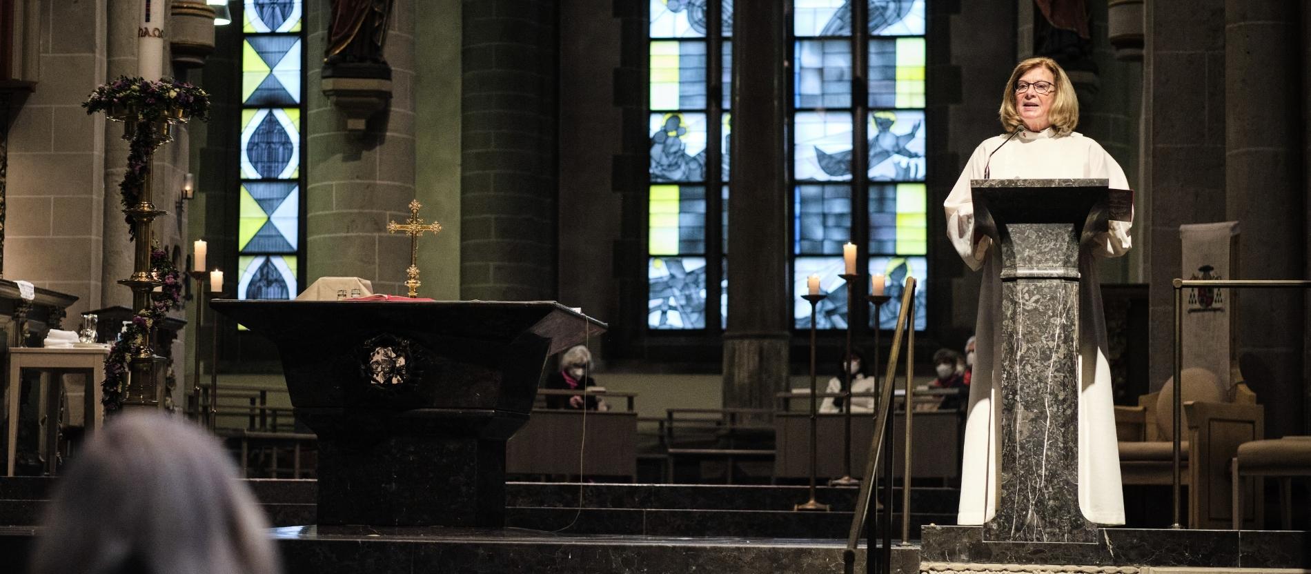 Eine Frau steht in liturgischer Kleidung am Ambo im Essener Dom und spricht