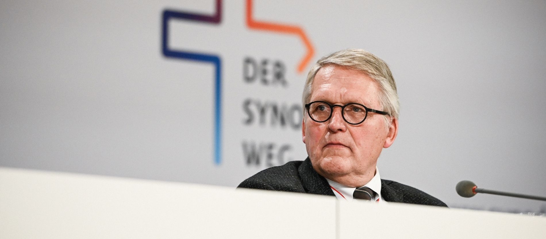 Thomas Sternberg sitzt vor einem Mikrofon, im Hintergrund das Logo des Synodalen Wegs.