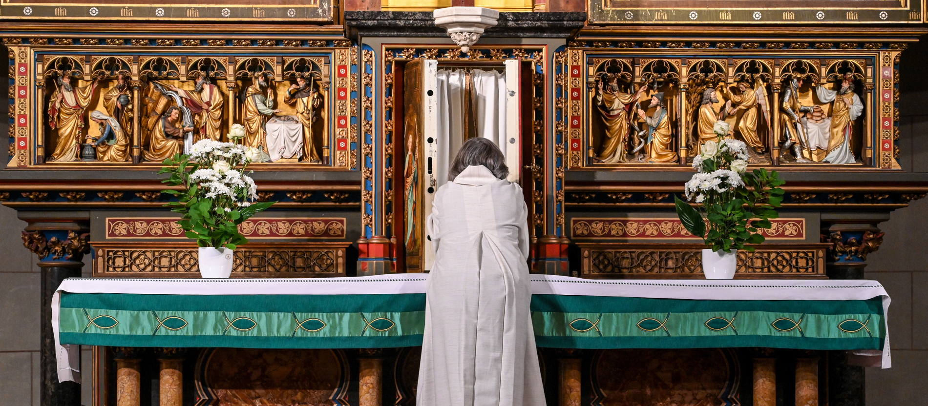 Eine Frau, Wortgottesdienstleiterin, in liturgischem Gewand steht vor dem geöffneten Tabernakel