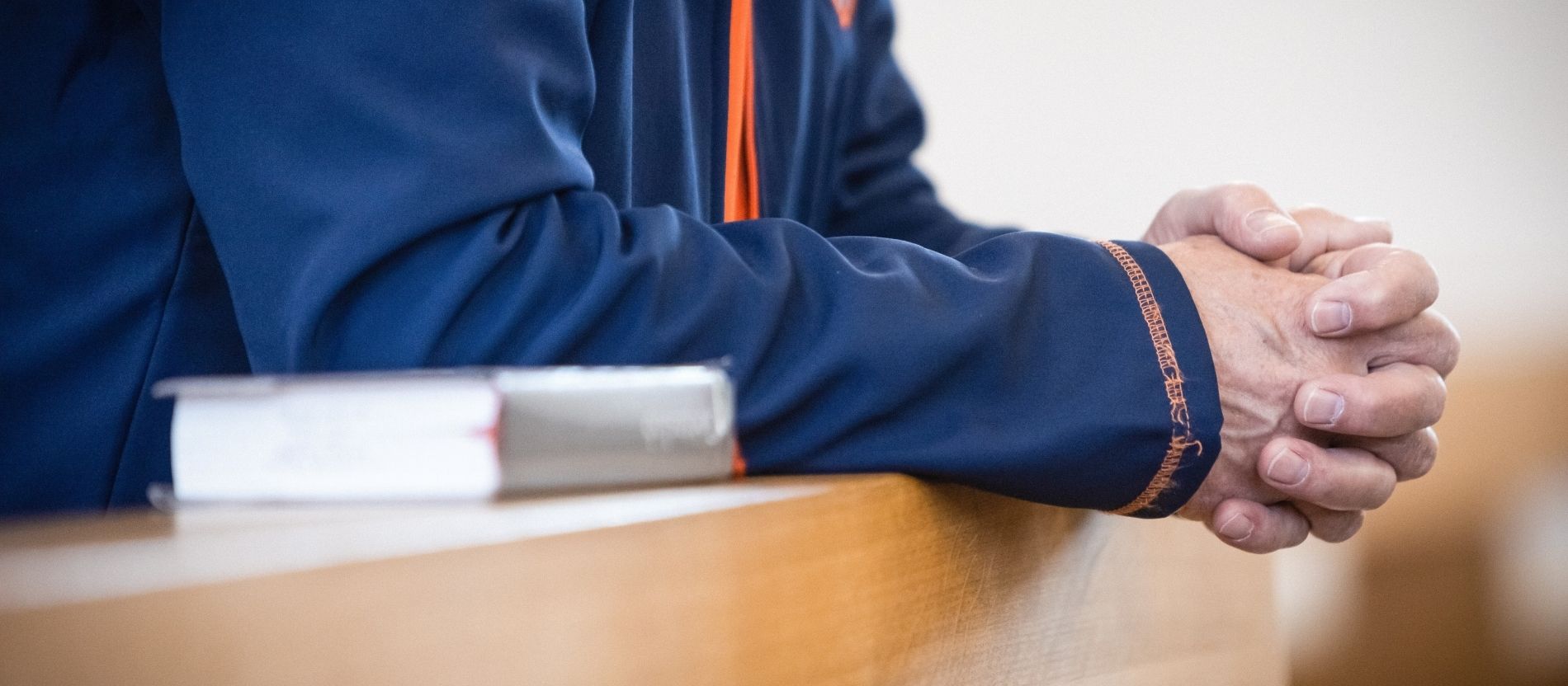 Ein Mann kniet in der Kirchenbank und hat die Hände zum Gebet gefaltet