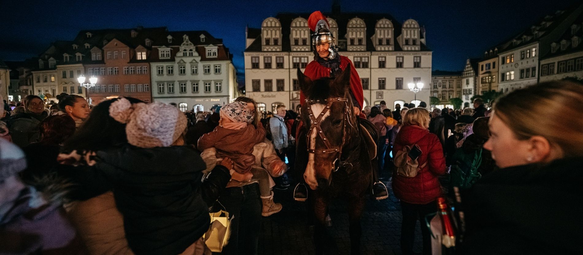 Erwachsene und Kinder stehen auf einem Marktplatz um einen als St. Martin verkleideten Mann herum