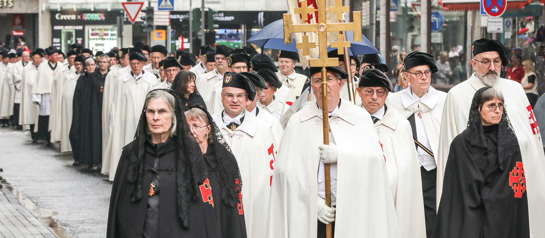 Prozession von schwarz gekleideten Frauen und weiß gekleideten Männern durch die Kölner Innenstadt