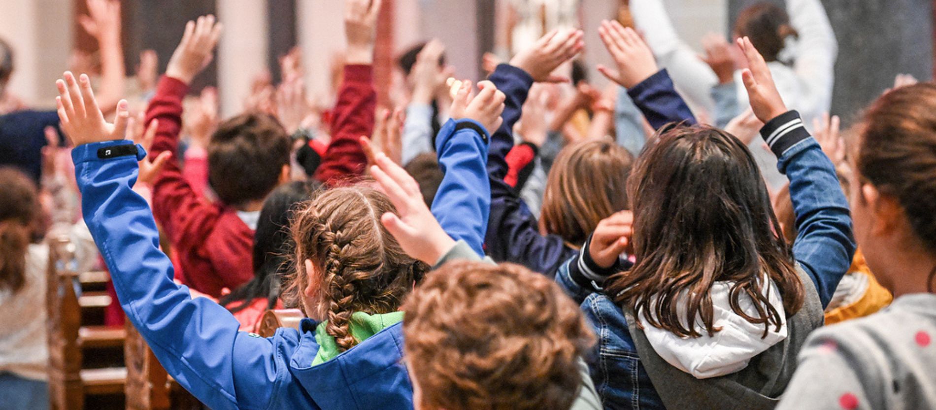 Kinder recken die Arme in die Höhe bei einem Lied in einem Gottesdienst.