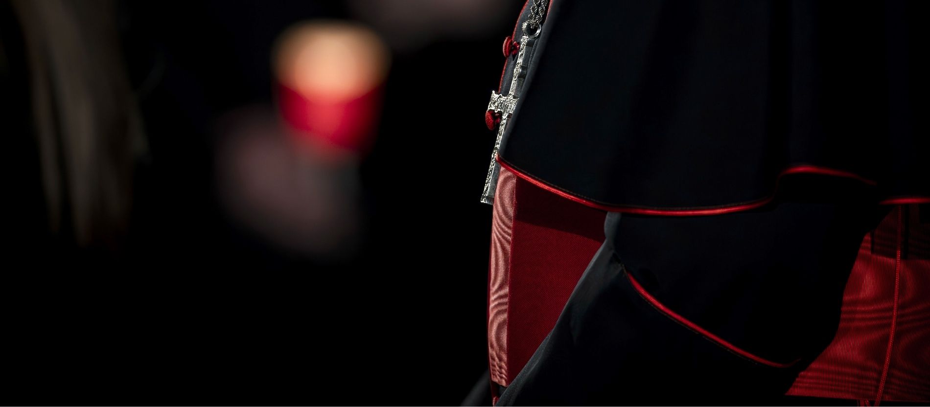 Kreuz und Soutane eines Kardinals vor dunklem Hintergrund